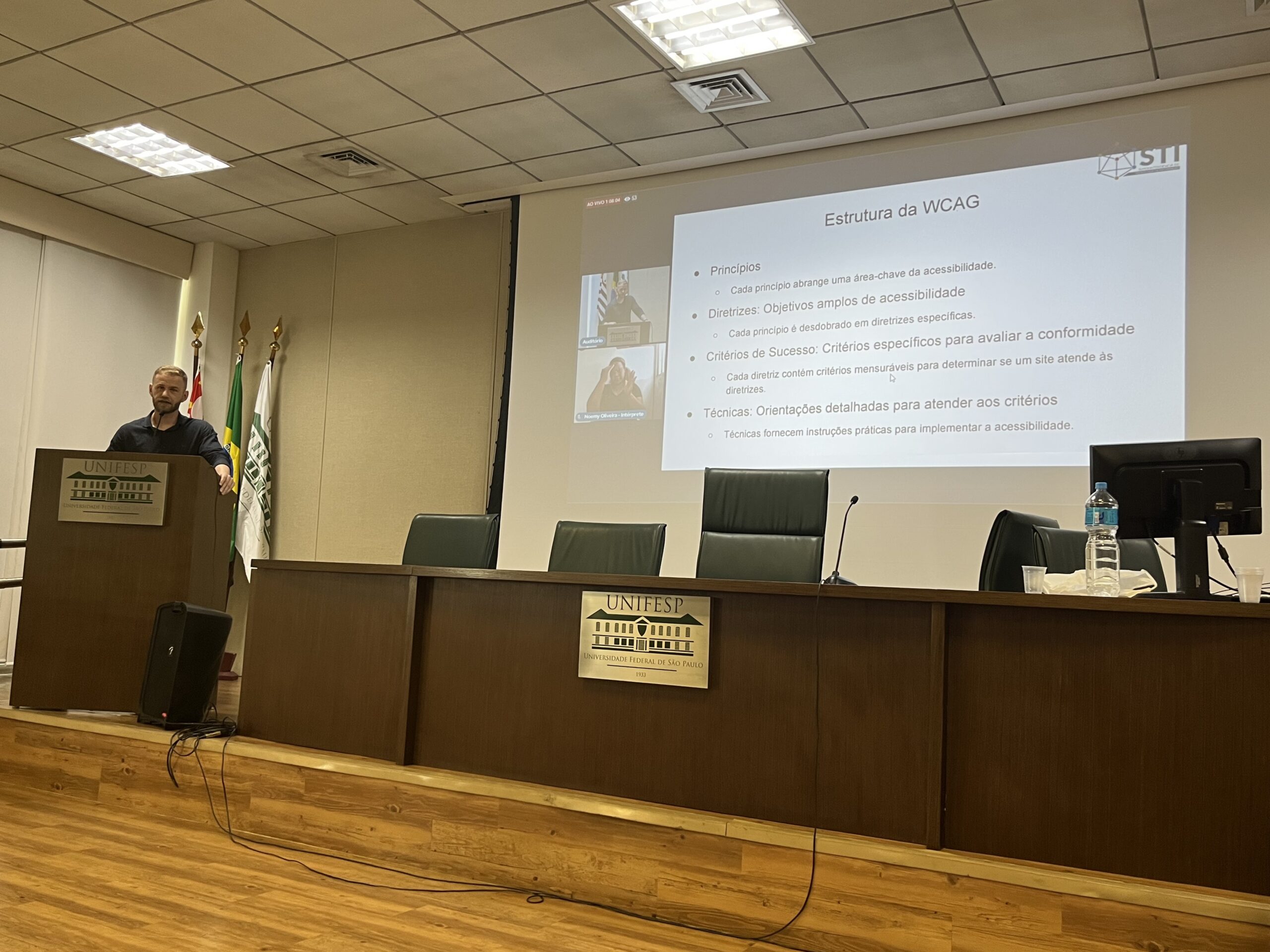 Cr&iacute;stian falando ao p&uacute;lpito em audit&oacute;rio, tendo ao lado a tela onde a apresenta&ccedil;&atilde;o est&aacute; projetada.