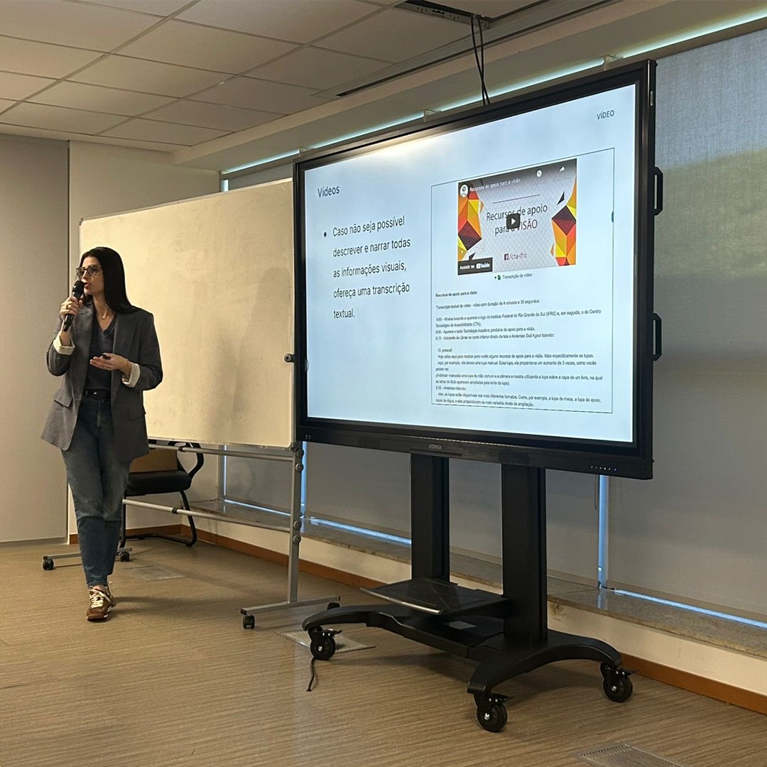 Mulher em pé fala ao lado de tela que exibe slide com texto e imagem