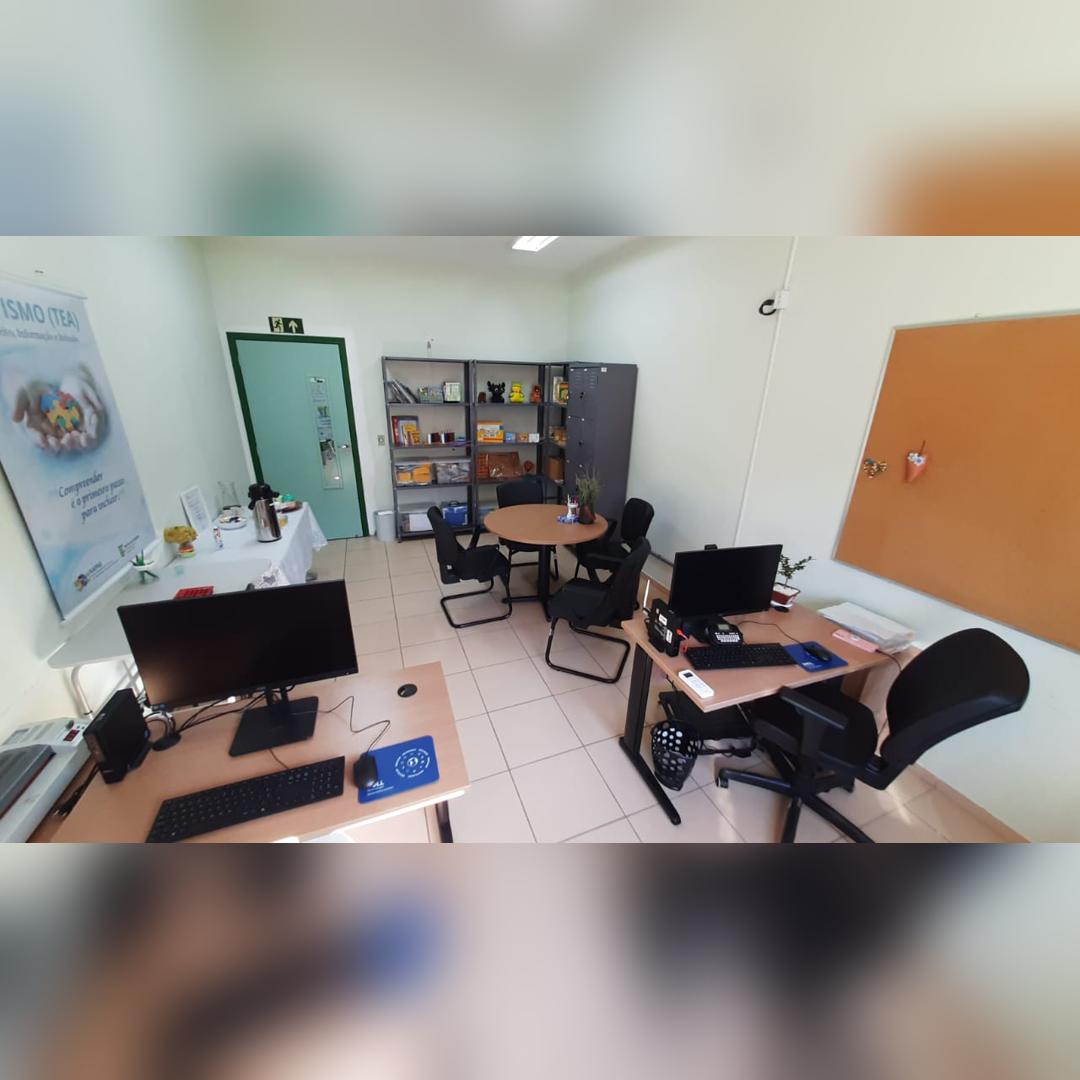 Sala com mesa, cadeiras, computador, monitor na parede e arm&aacute;rios ao fund
